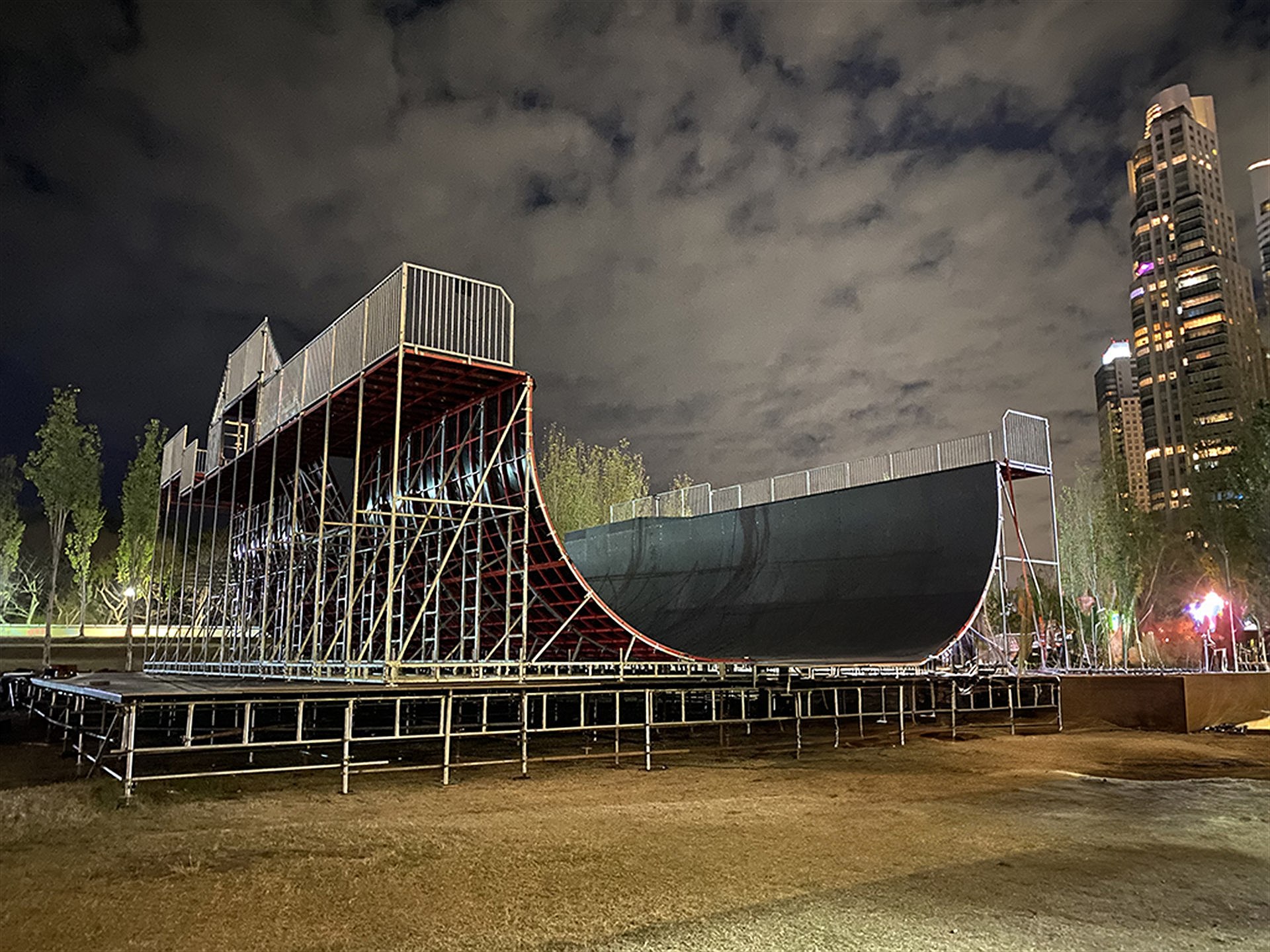 Portable vert ramp on a scaffold deck, floodlit at night against a city skyline